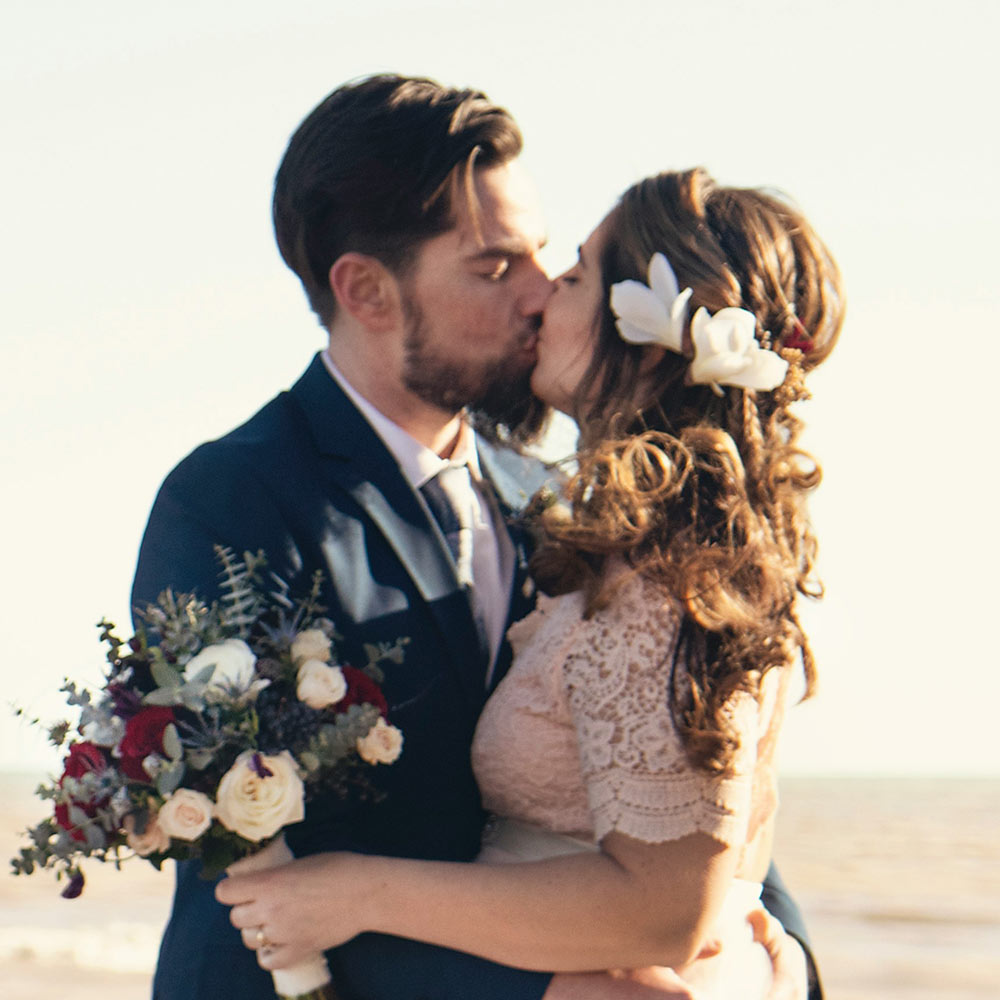 Newlyweds kissing beside the ocean